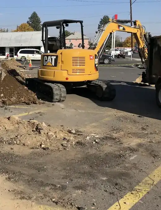 Excavators and a pile of dug soil in a commercial parking lot