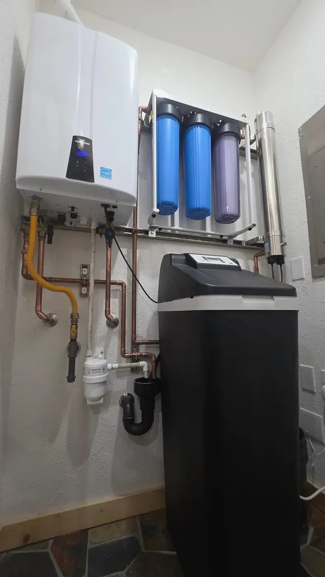 A wall-hung tankless heater, two filter housings and a water softener installed on one wall with gas and copper lines
