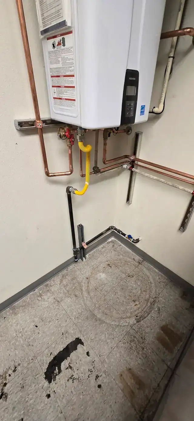 A closer view of a wall-hung tankless heater install with copper and gas lines in a utility closet