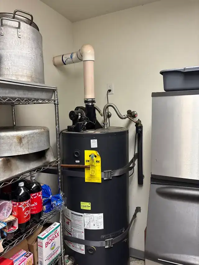 A tank water heater in a restaurant storeroom with shelves of stock behind it