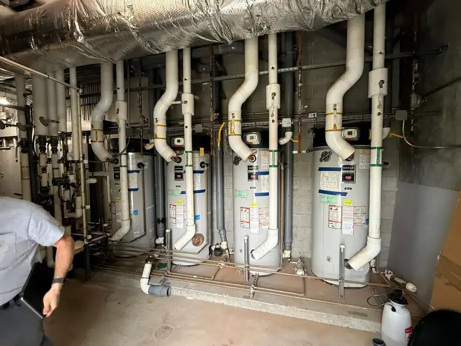 A commercial mechanical room with four gas storage water heaters, white PVC venting and copper headers