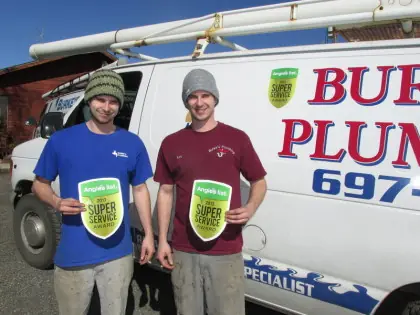 Twins Ken and Steve Burke holding Angie's List Super Service decals in front of a white Burke's Plumbing van